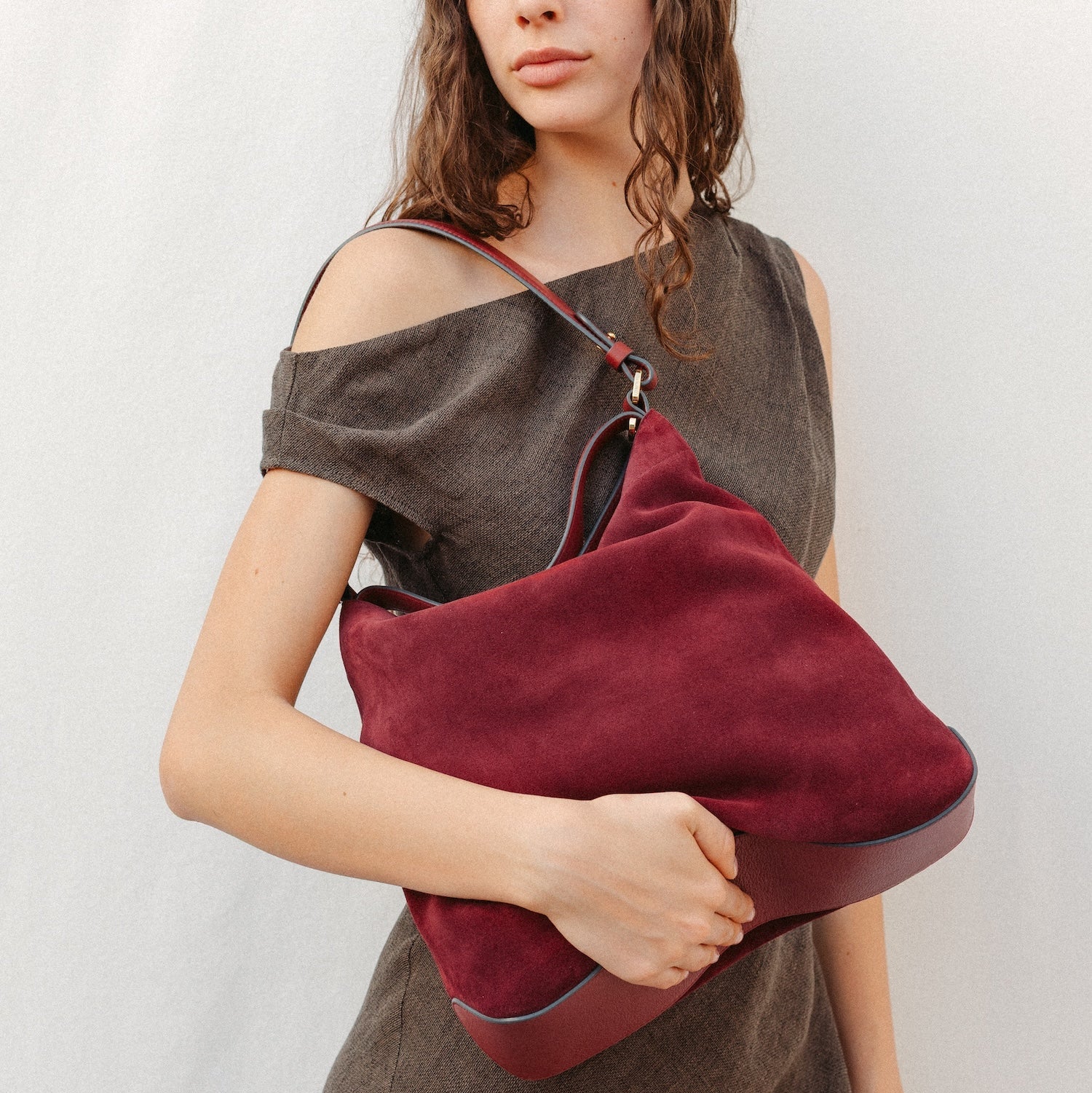 Model wearing STOW London's Curve in Burgundy suede leather featuring the detachable shoulder strap with gold hardware