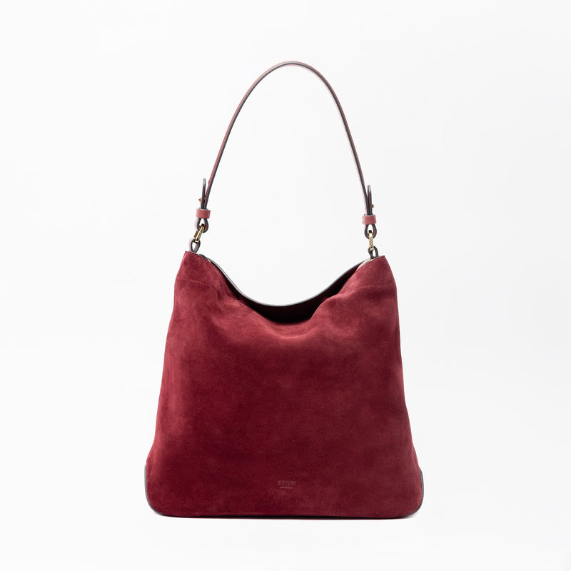 STOW London's Curve in Burgundy suede leather on a light grey background featuring the detachable shoulder strap with gold hardware