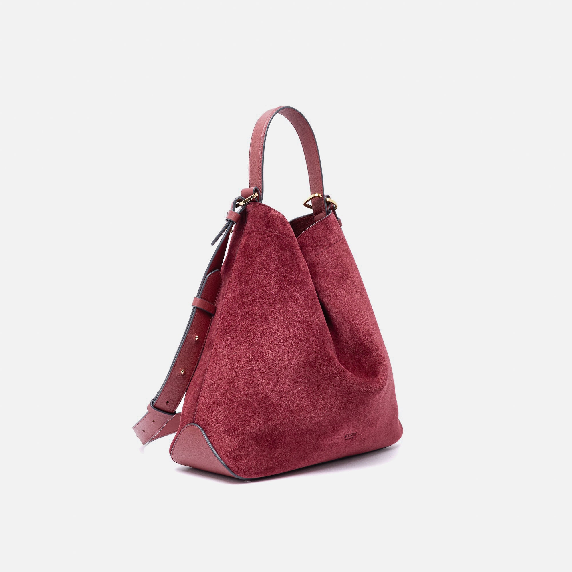 Off-axis view of Stow London's Curve bag in Burgundy suede leather shaped in a triangular form featuring gold-coated stainless steel hardware on a light grey background