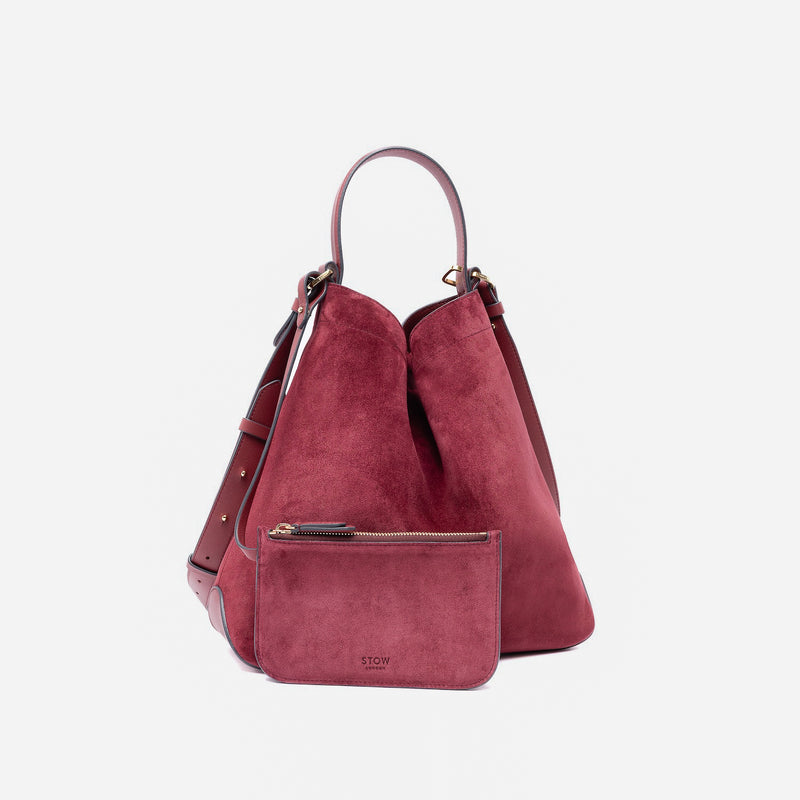 Stow London's Curve bag and matching, detachable interior pouch in Burgundy suede leather featuring gold-coated stainless steel hardware on a light grey background