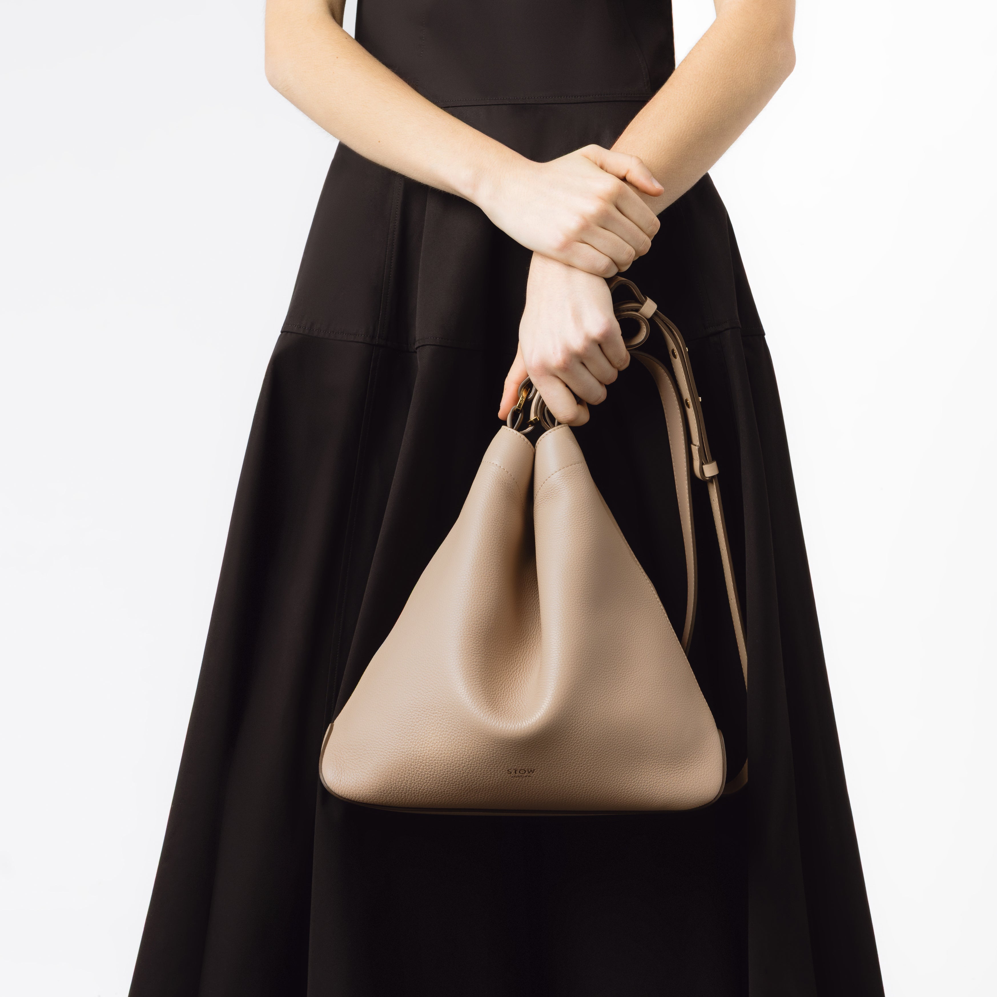 Model holding STOW London's Curve bag in Camel pebbled leather on a white background