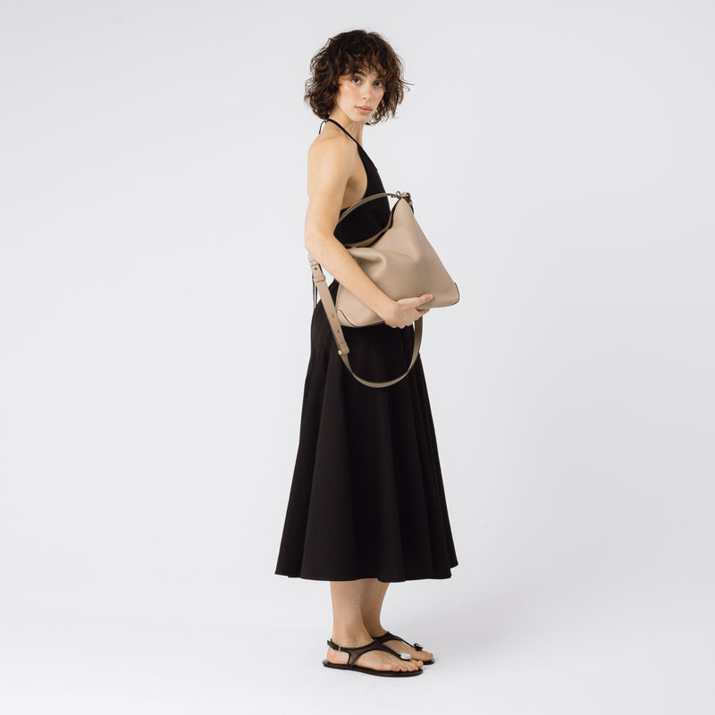 Model holding STOW London's Curve bag in Camel pebbled leather on a white background
