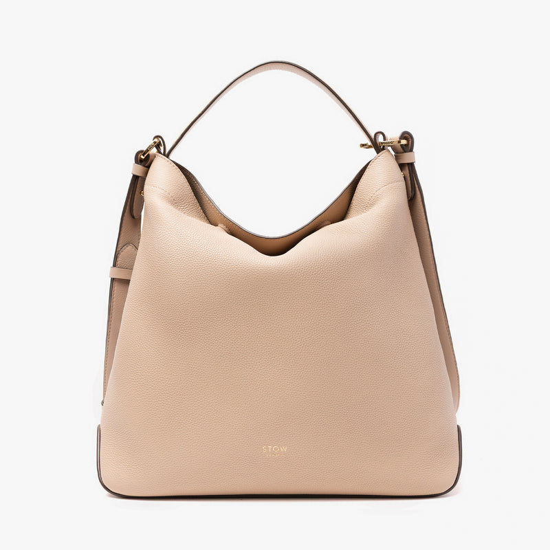 Stow London's Curve bag in Camel pebbled leather featuring gold-coated stainless steel hardware on a light grey background