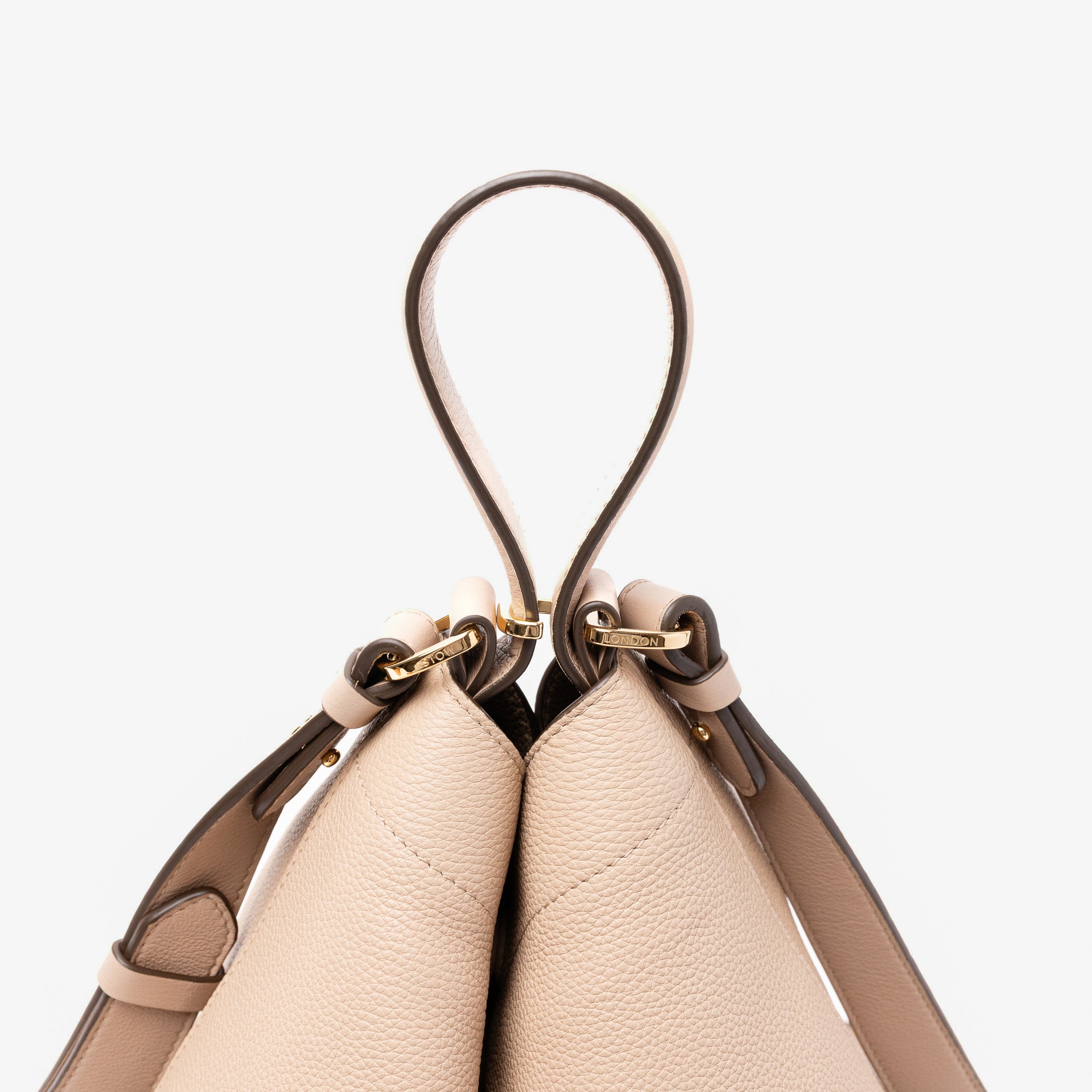 Close up of the handle on Stow London's Curve bag in Camel pebbled leather featuring gold-coated stainless steel hardware and clip and detachable strap on a light grey background