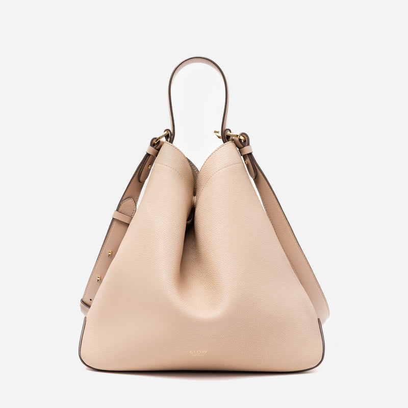 Stow London's Curve bag in Camel pebbled leather shaped in a triangular form featuring gold-coated stainless steel hardware on a light grey background