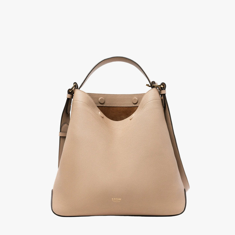 STOW London's Curve bag in Camel pebbled leather featuring gold-coated stainless steel hardware on a light grey background