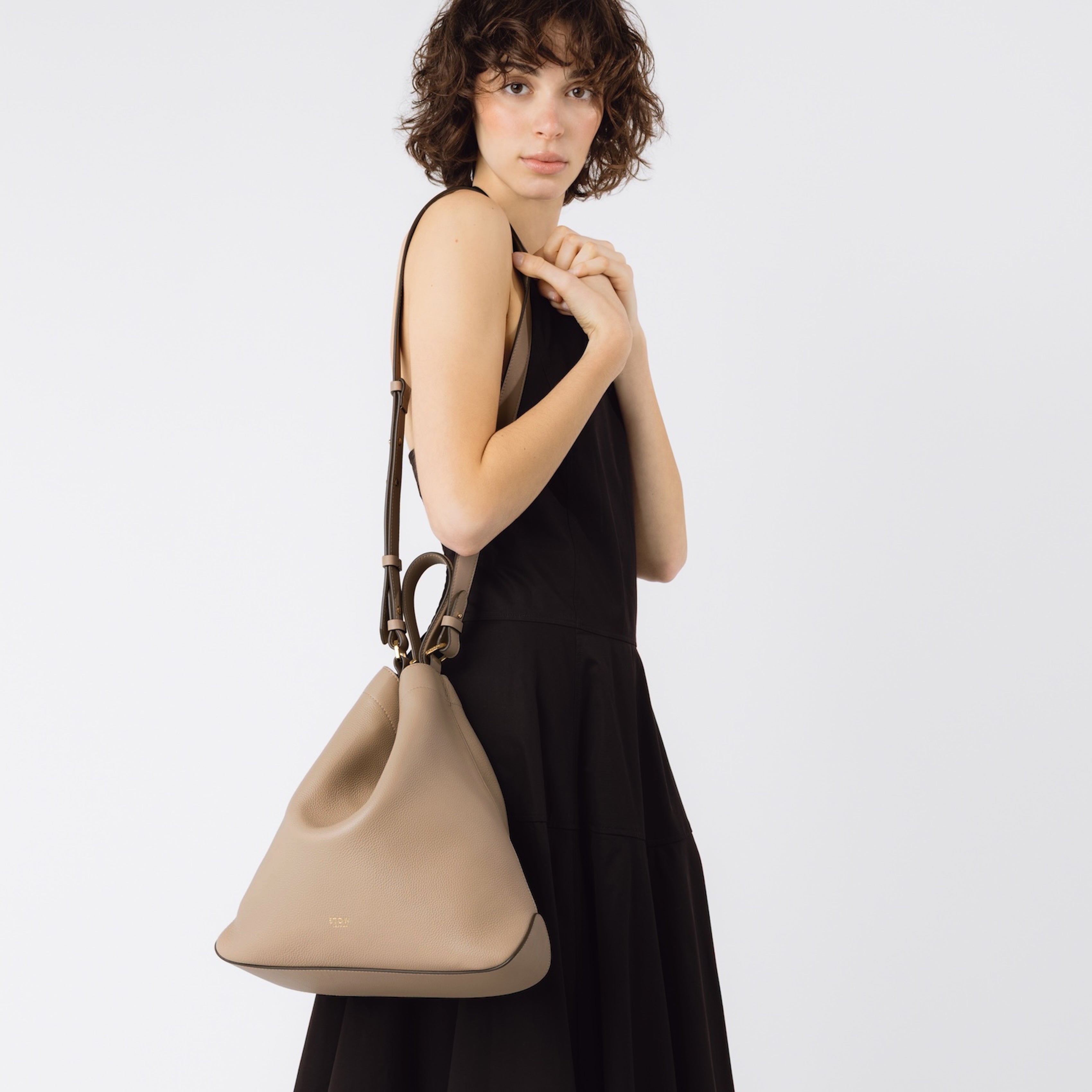 Model wearing STOW London's Curve bag in Camel pebbled leather on her shoulder on a white background