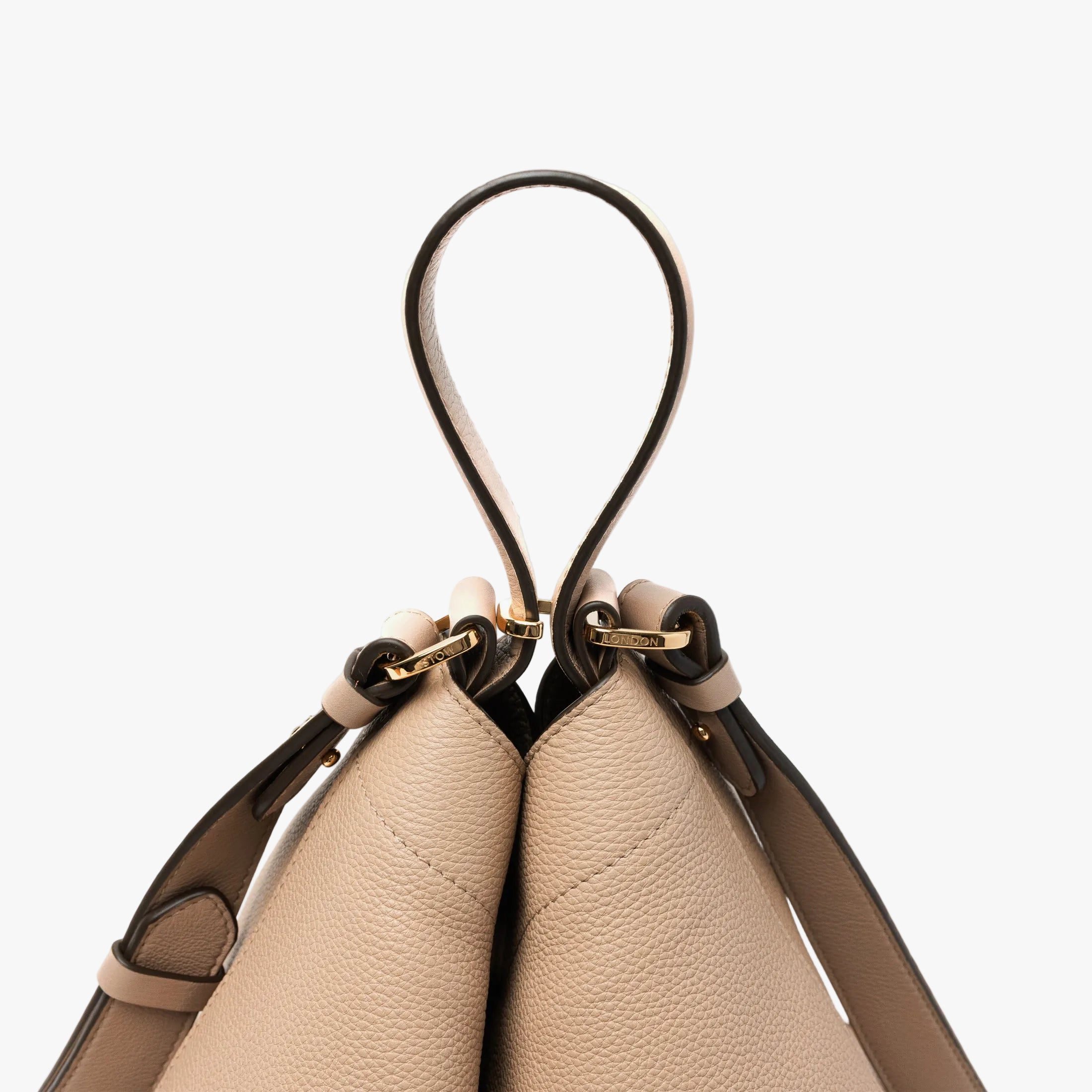 Close up of top handle on STOW London's Curve bag in Camel pebbled leather featuring gold-coated stainless steel hardware and its detachable crossbody strap on a light grey background