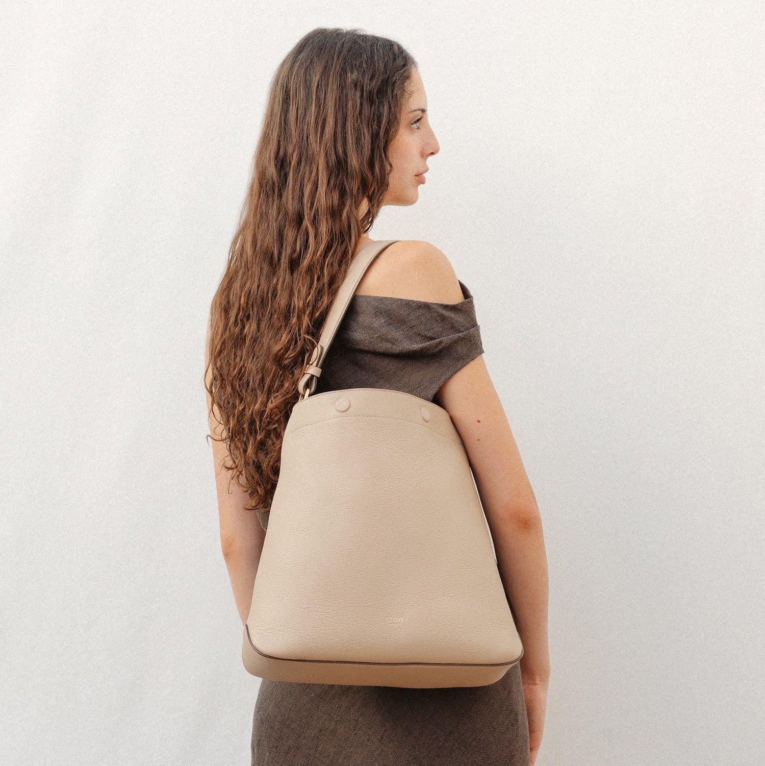 Model wearing STOW London's Curve in Camel leather featuring the detachable shoulder strap, top handle with gold hardware and details 