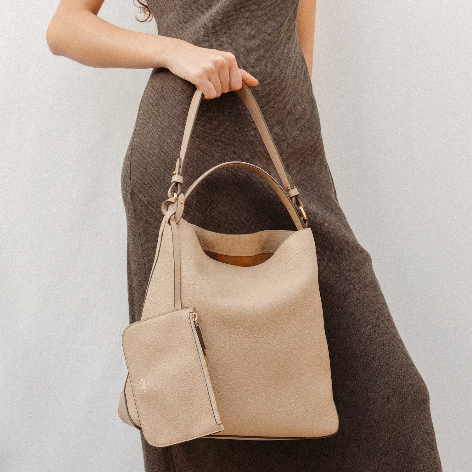 Model holding STOW London's Curve in Camel leather featuring the detachable shoulder strap, top handle and interior pouch with gold hardware and details 
