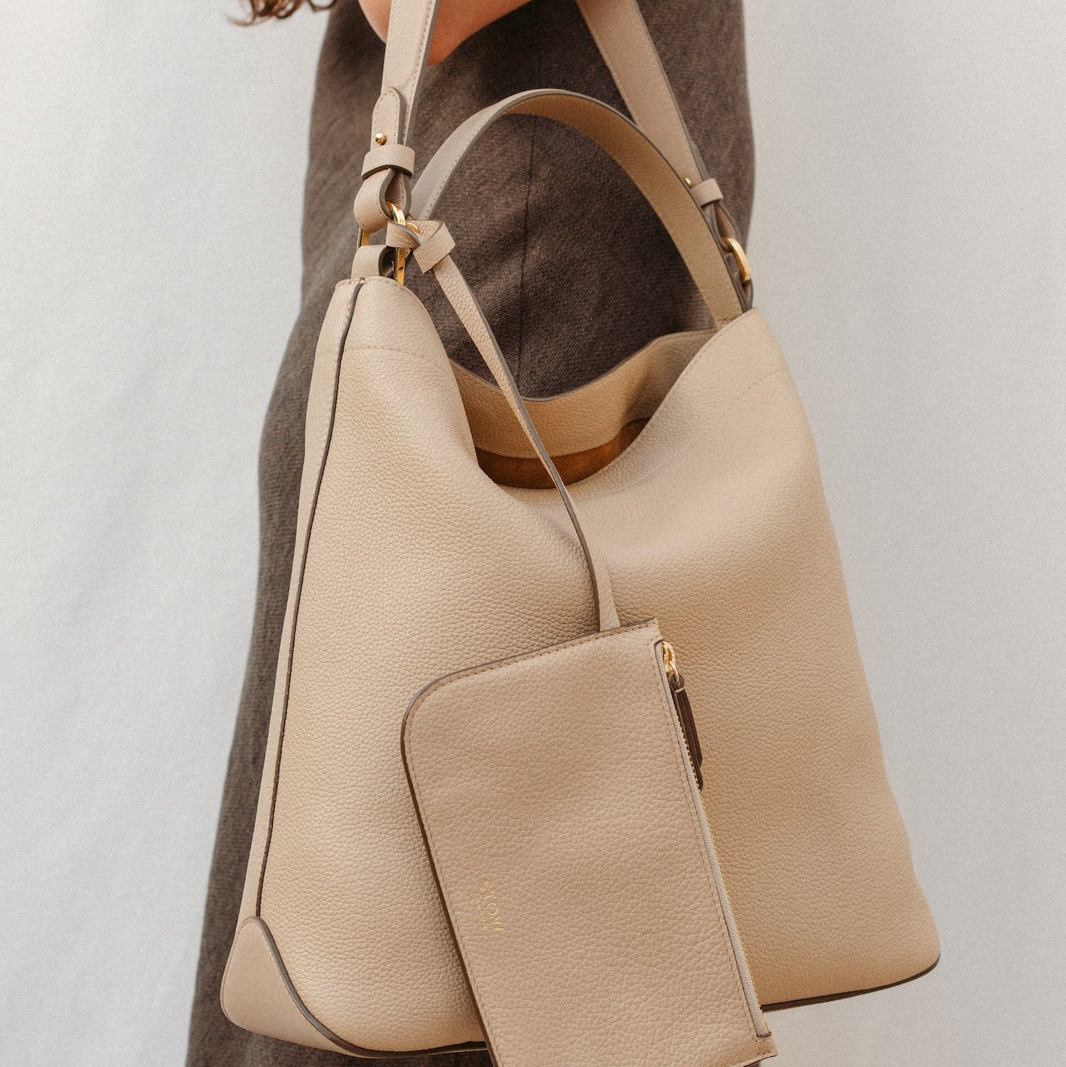 Model wearing STOW London's Curve in Camel leather featuring the detachable shoulder strap, top handle and interior pouch with gold hardware and details 