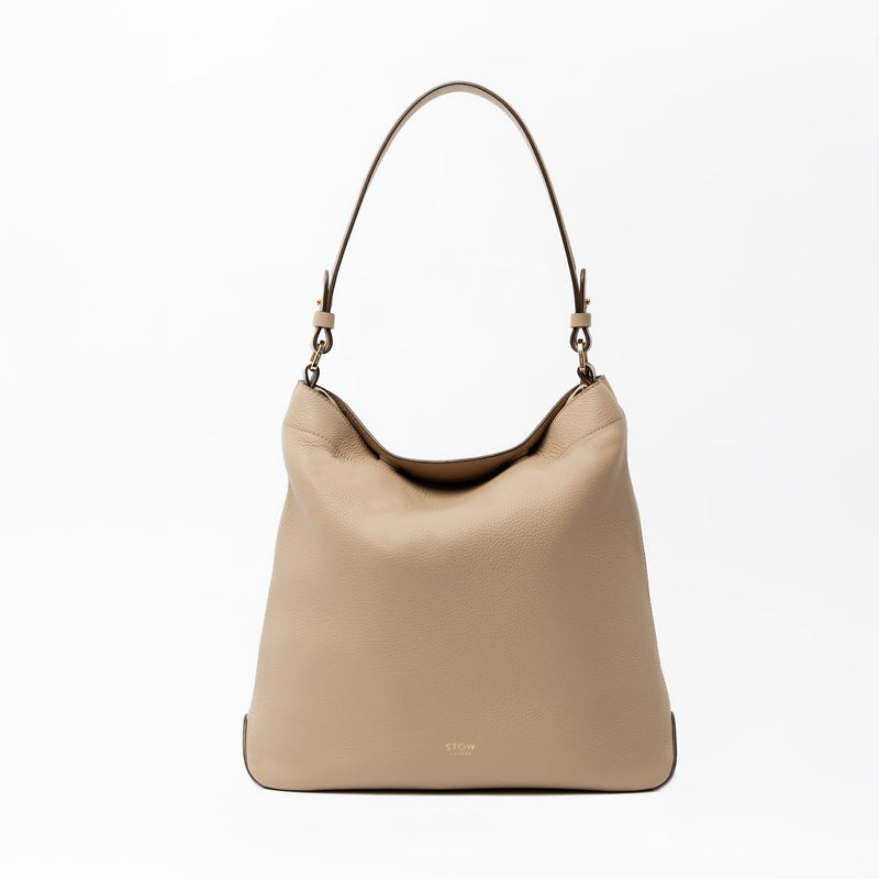 STOW London's Curve in Camel leather on a light grey background featuring the detachable shoulder strap with gold hardware and details 