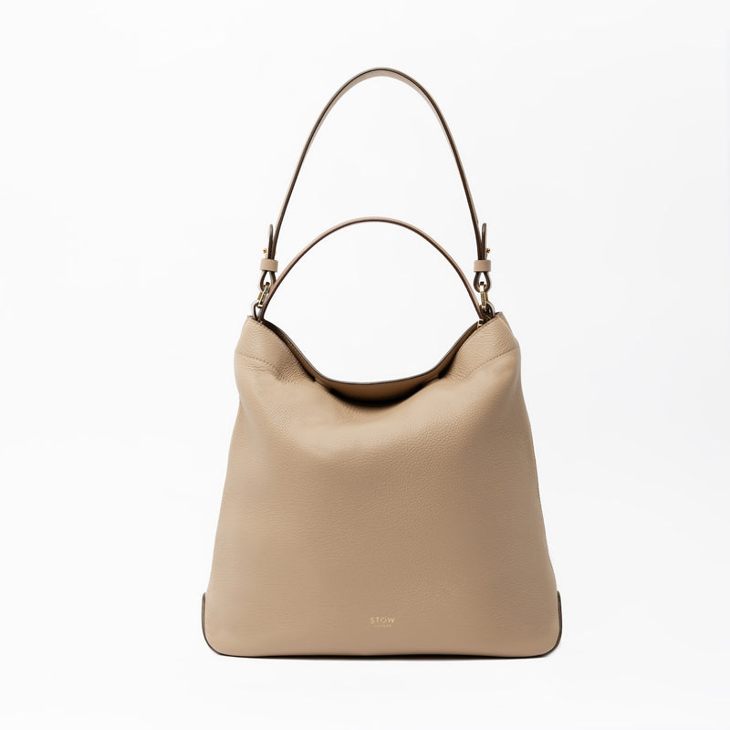 STOW London's Curve in Camel leather on a light grey background featuring the detachable shoulder strap and top handle with gold hardware and details 