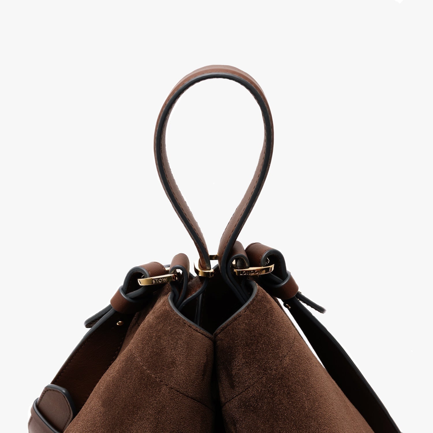 Close up of the handle of STOW London's Curve bag in Chocolate suede leather featuring gold-coated stainless steel hardware and detachable crossbody strap on a light grey background