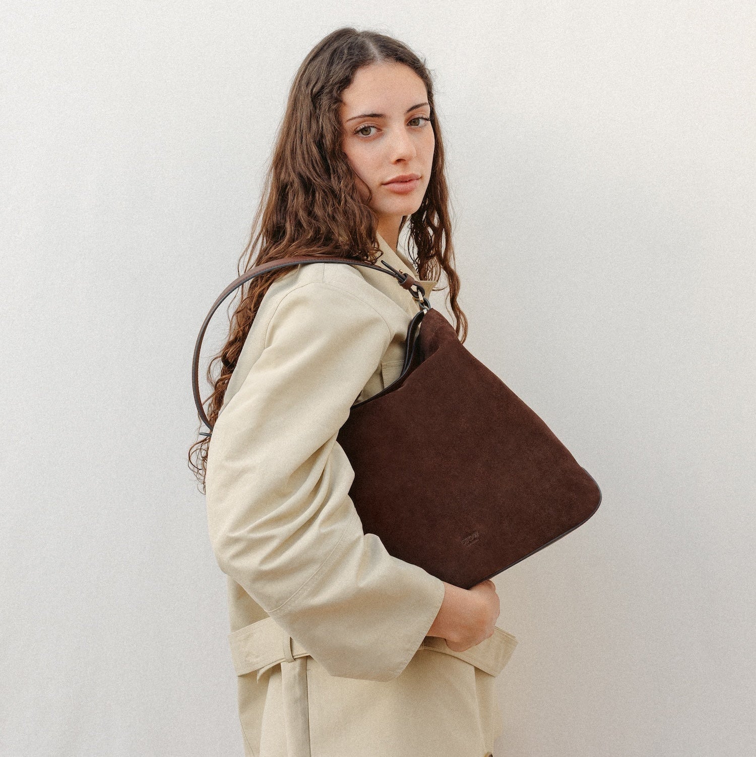 Model wearing STOW London's Curve in Chocolate Suede leather featuring the detachable shoulder strap with gold hardware