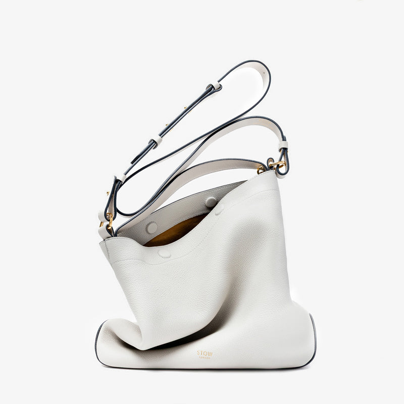 Stow London's Curve bag in Cloud Grey pebbled leather featuring gold-coated stainless steel hardware on a light grey background