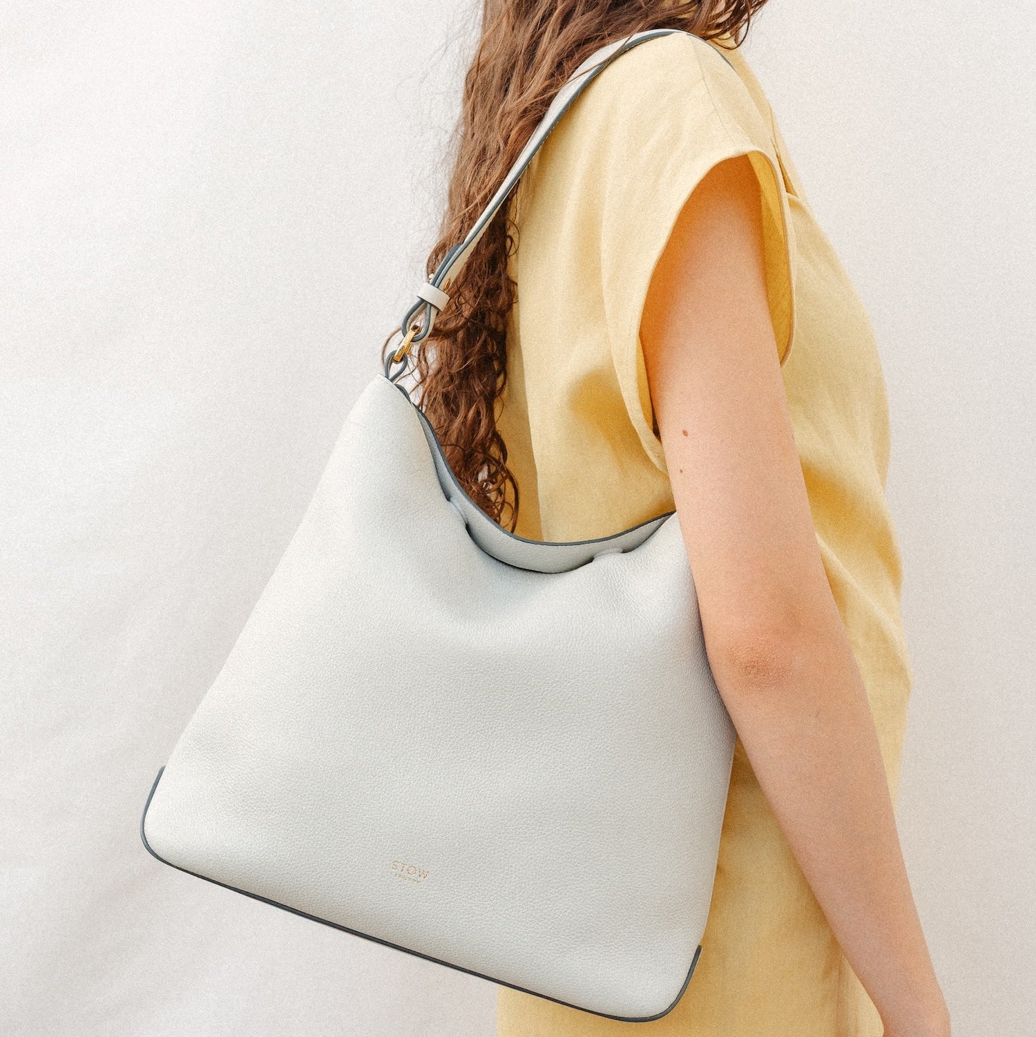 Model wearing STOW London's Curve in Cloud Grey leather featuring the detachable shoulder strap with gold hardware and details 
