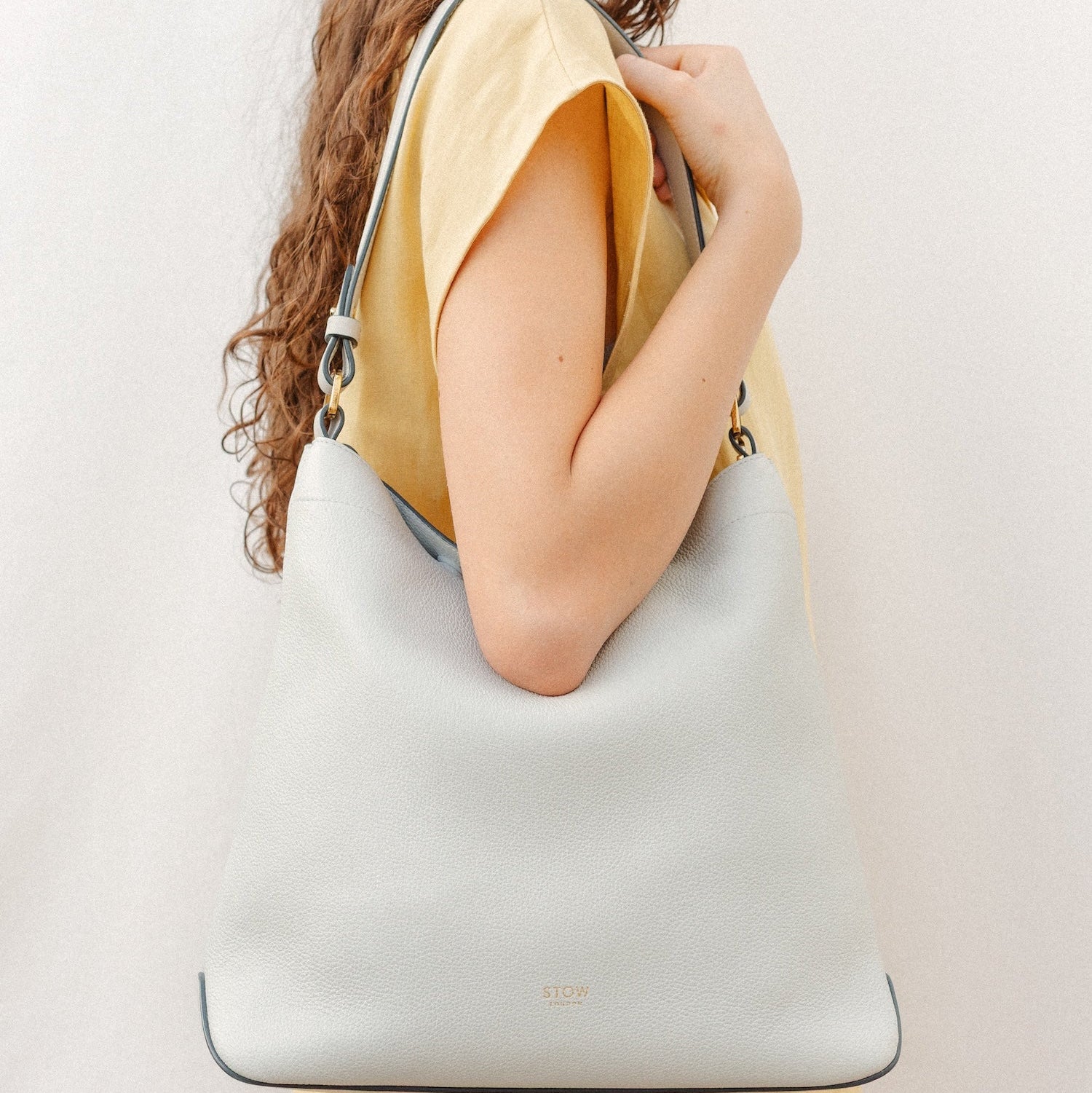 Model wearing STOW London's Curve in Mocha leather featuring the detachable shoulder strap with gold hardware and details 