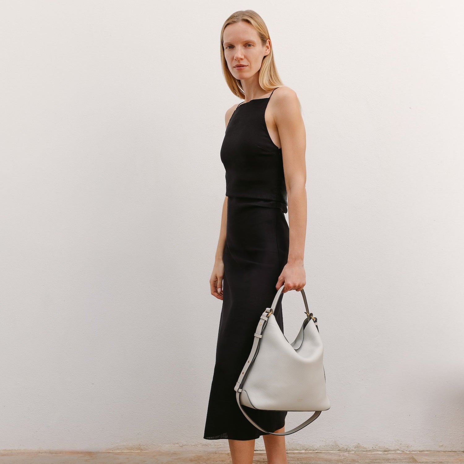 Model with STOW London's Curve bag in Cloud Grey pebbled leather featuring gold-coated stainless steel hardware 