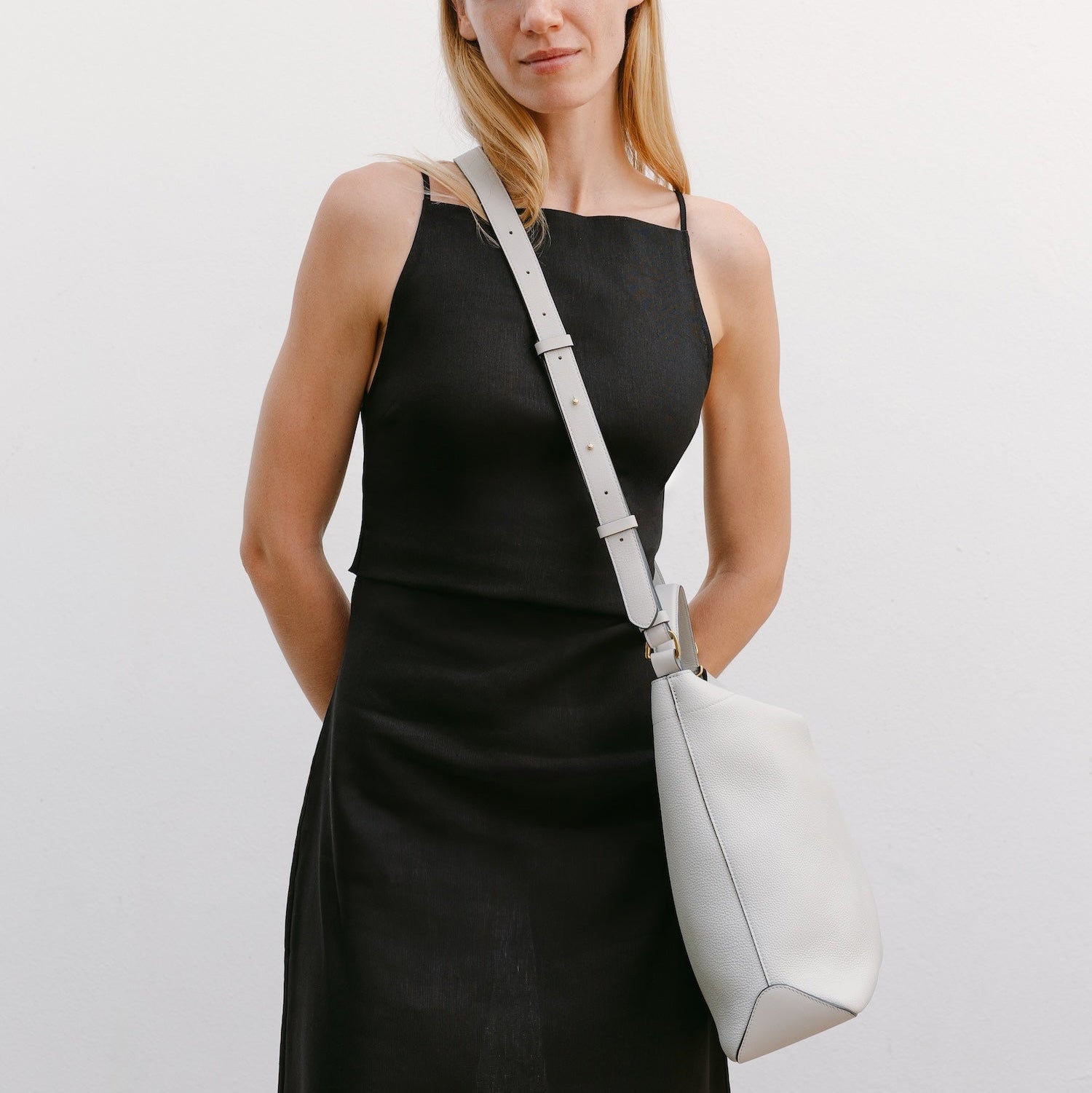 Model wearing STOW London's Curve bag in Cloud Grey pebbled leather crossbody featuring gold-coated stainless steel hardware 