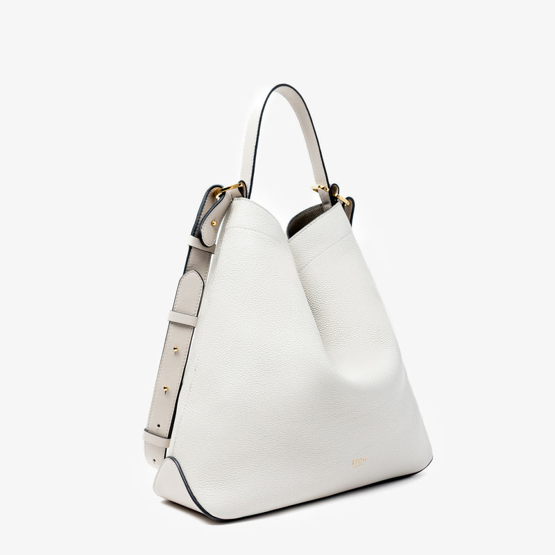 Off-axis shot of Stow London's Curve bag in Cloud Grey pebbled leather in a triangular shape featuring gold-coated stainless steel hardware on a light grey background
