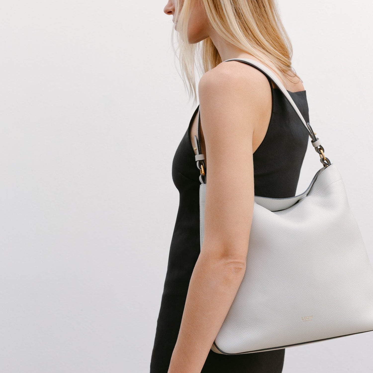 Model wearing STOW London's Curve in Cloud Grey leather featuring the detachable shoulder strap with gold hardware and details 