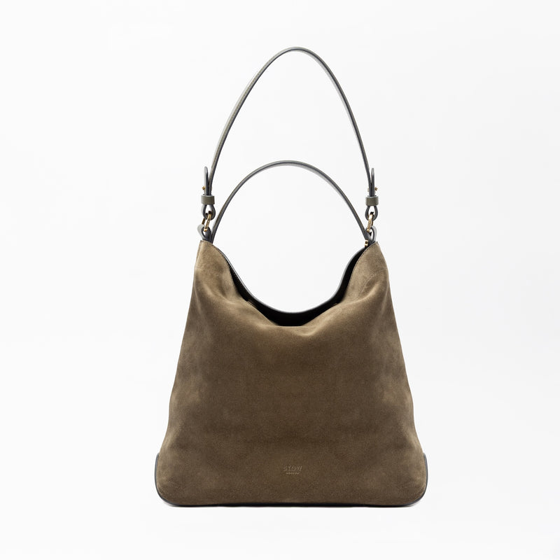 STOW London's Curve in Dark Green suede leather on a light grey background featuring the detachable shoulder strap and top handle with gold hardware