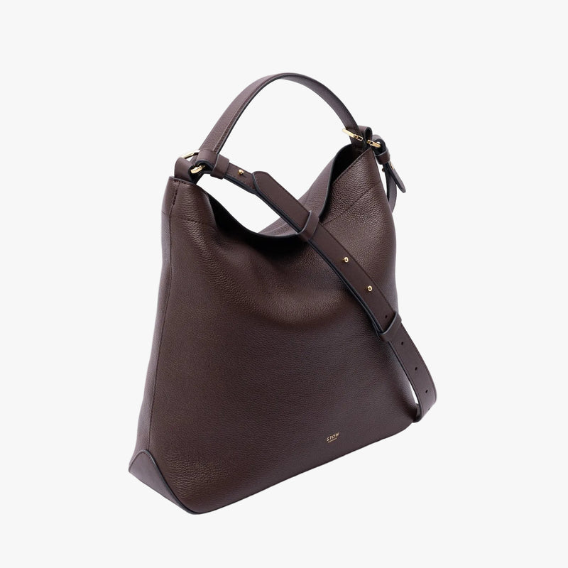Off-axis view of STOW London's Curve in Espresso pebbled leather featuring the detachable crossbody strap and gold-coated stainless steel hardware on a light grey background
