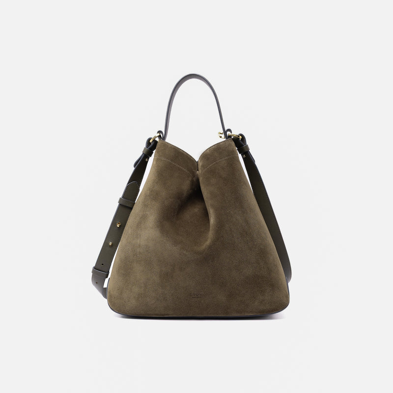 Stow London's Curve bag in Dark Green suede leather shaped in a triangular form featuring gold-coated stainless steel hardware on a light grey background
