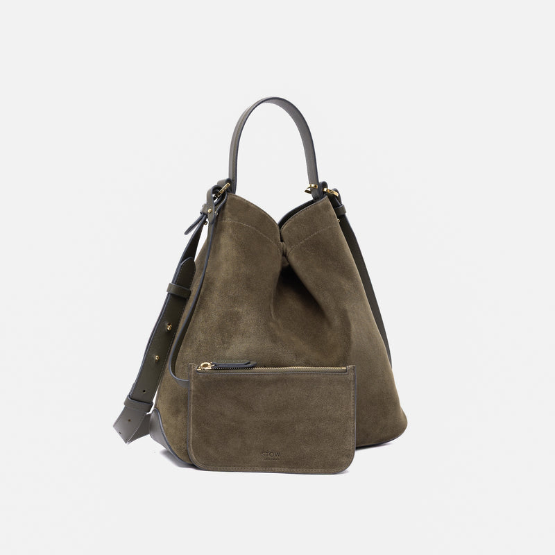 Stow London's Curve bag in Dark Green suede leather featuring its matching detachable interior pouch and gold-coated stainless steel hardware on a light grey background