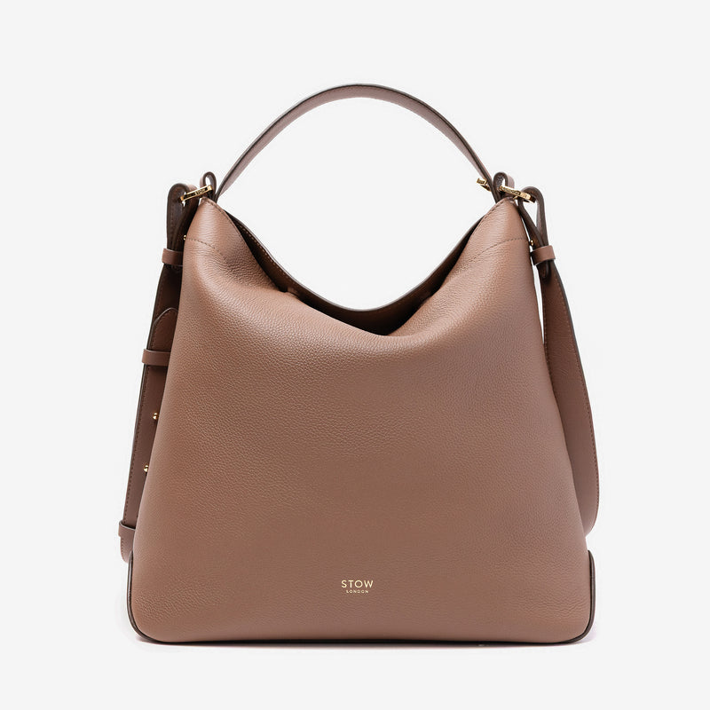 Stow London's Curve bag in Mocha pebbled leather featuring gold-coated stainless steel hardware on a light grey background