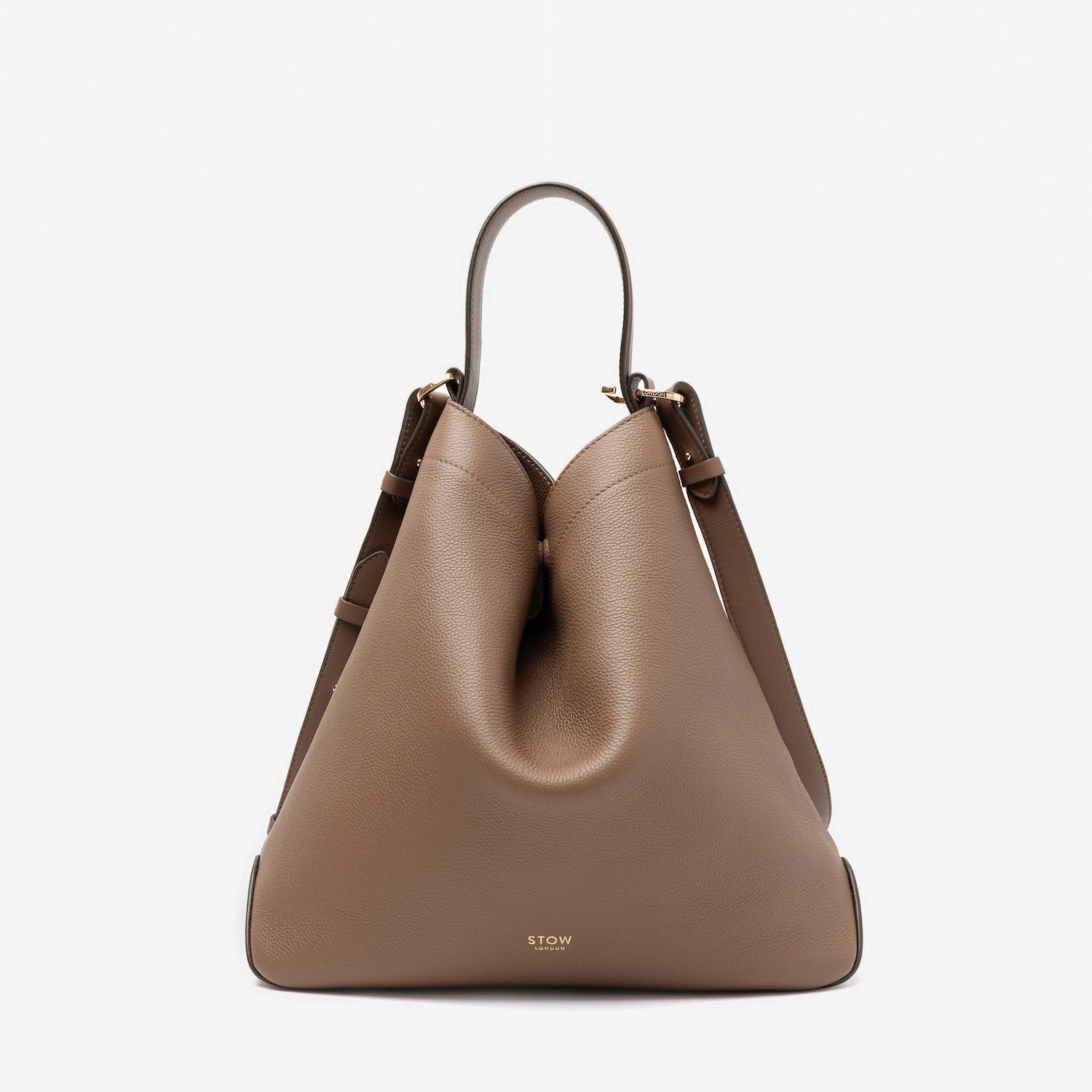 STOW London's Curve bag in Mocha pebbled leather shaped in a triangular form featuring gold-coated stainless steel hardware on a light grey background