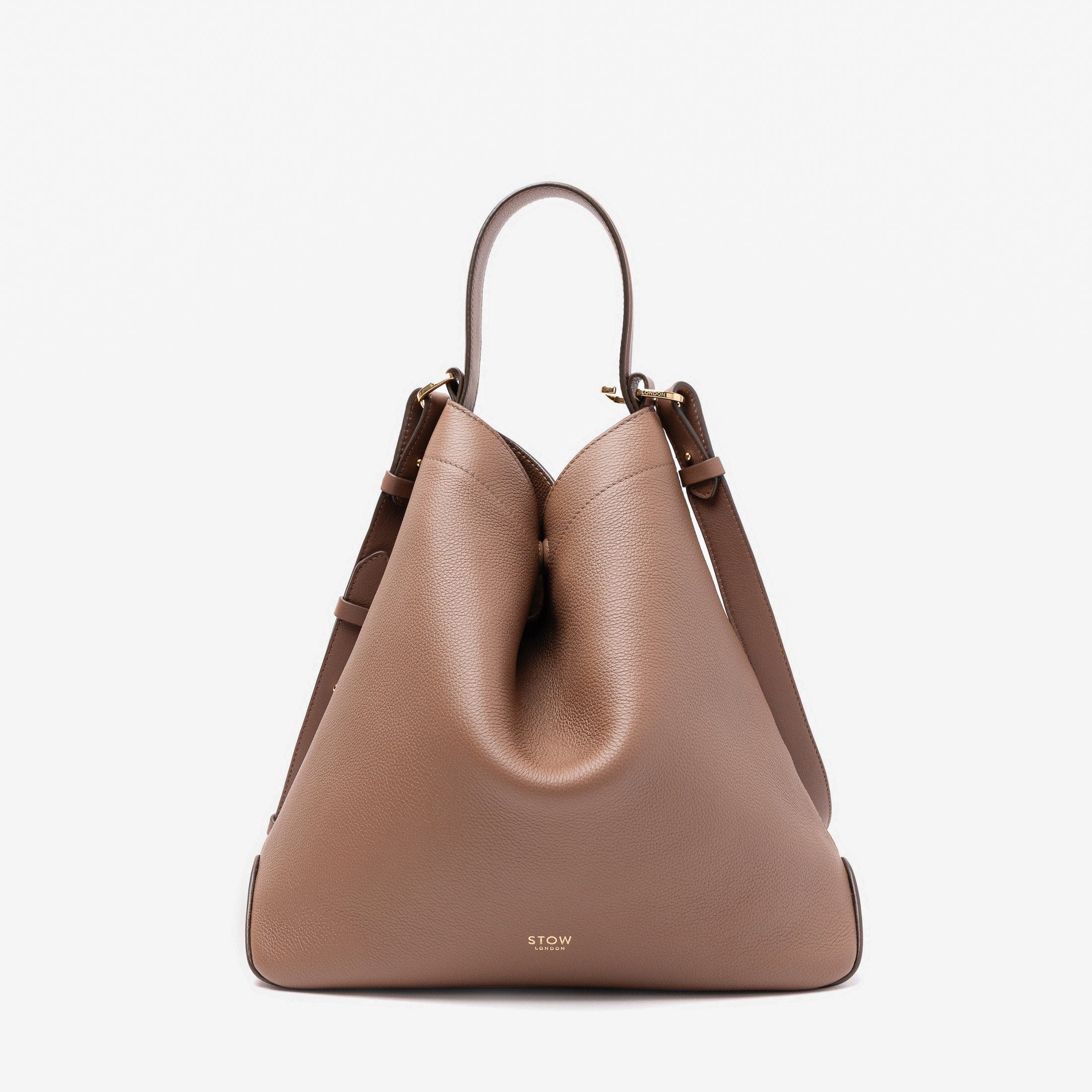 Stow London's Curve bag in Mocha pebbled leather shaped in a triangular form featuring gold-coated stainless steel hardware on a light grey background