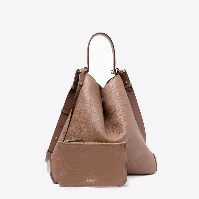 Stow London's Curve bag in Mocha pebbled leather and matching, detachable interior pouch featuring gold-coated stainless steel hardware on a light grey background
