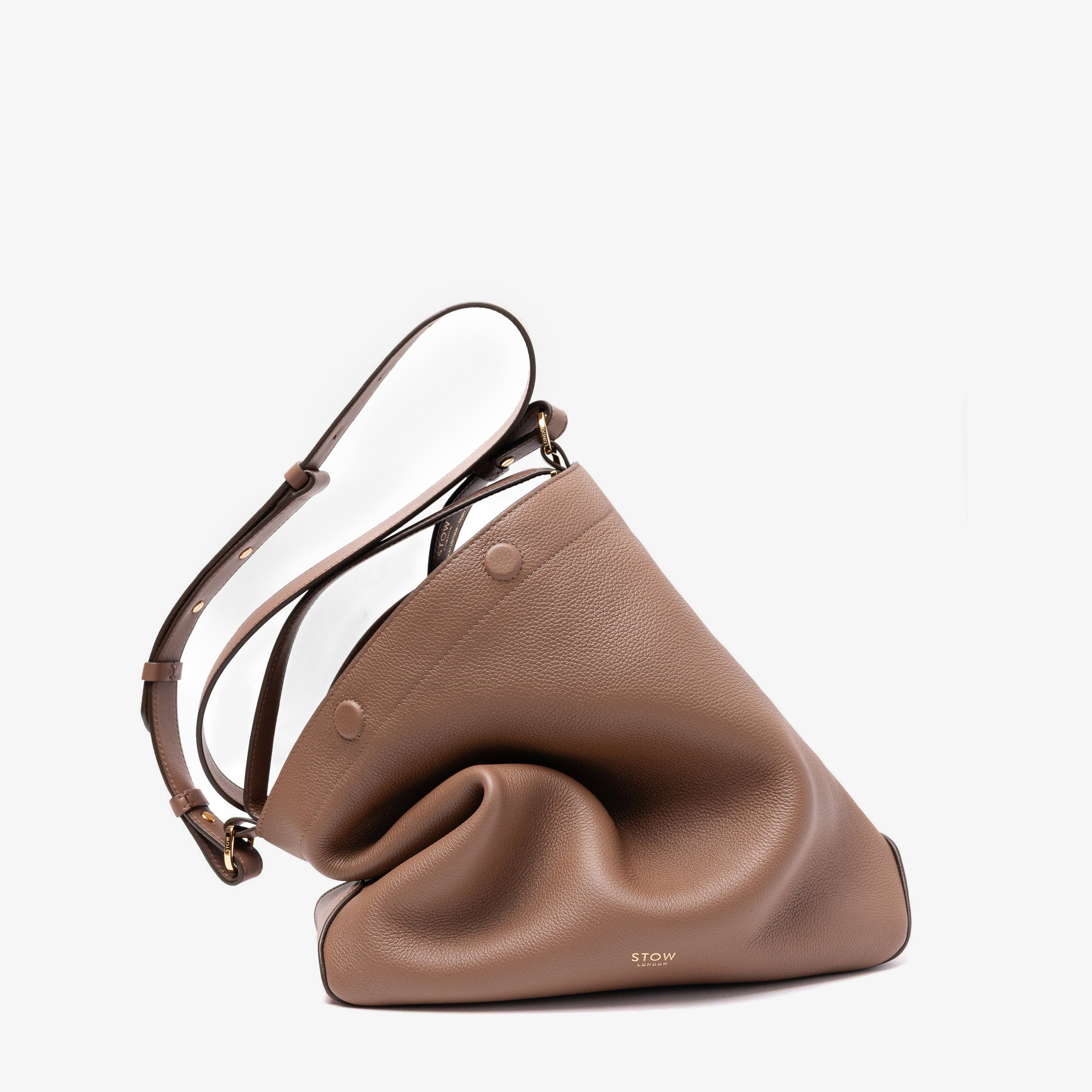Stow London's Curve bag and detachable crossbody strap in Mocha pebbled leather featuring gold-coated stainless steel hardware on a light grey background