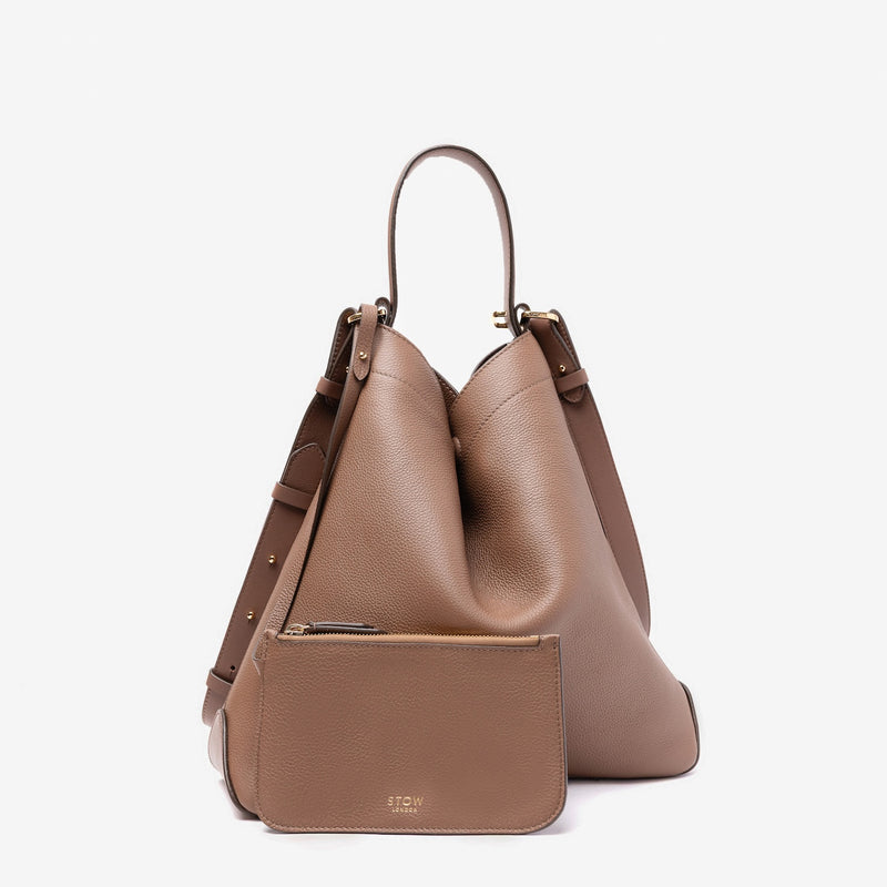 Stow London's Curve bag in Mocha pebbled leather and matching, detachable interior pouch featuring gold-coated stainless steel hardware on a light grey background
