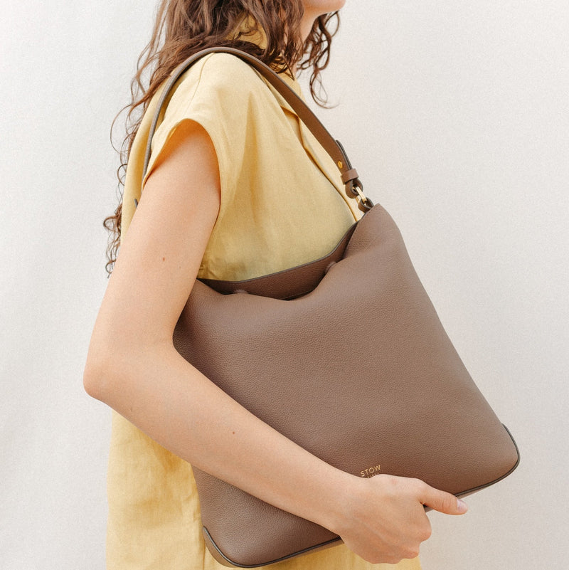 Model wearing STOW London's Curve in Mocha leather featuring the detachable shoulder strap with gold hardware and details 
