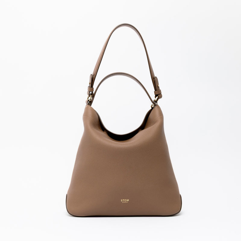 STOW London's Curve in Mocha leather on a light grey background featuring the detachable shoulder strap and top handle with gold hardware and details 