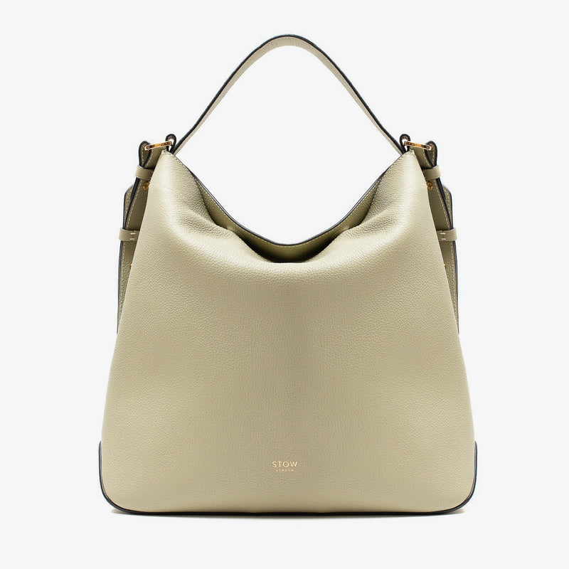 Stow London's Curve bag in Pale Green pebbled leather featuring gold-coated stainless steel hardware on a light grey background