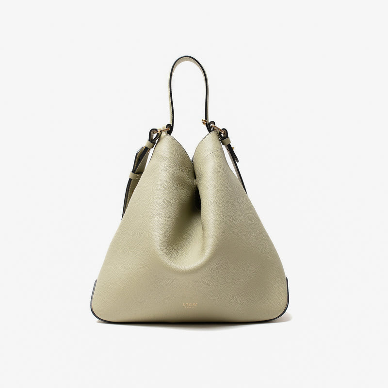 Stow London's Curve bag in Pale Green pebbled leather shaped in a triangular form featuring gold-coated stainless steel hardware on a light grey background