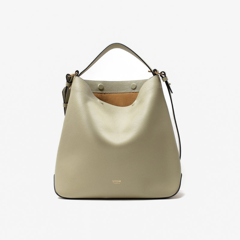 Stow London's Curve bag in Pale Green pebbled leather with magnets open featuring gold-coated stainless steel hardware on a light grey background