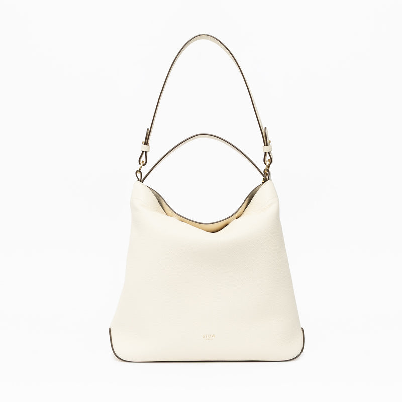 STOW London's Curve in Spring Moon leather on a light grey background featuring the detachable shoulder strap and top handle with gold hardware and details 