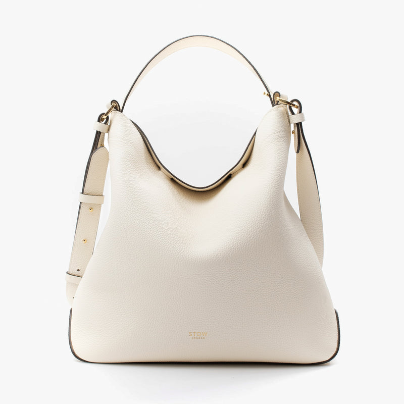 Stow London's Curve bag in Spring Moon pebbled leather featuring gold-coated stainless steel hardware on a light grey background