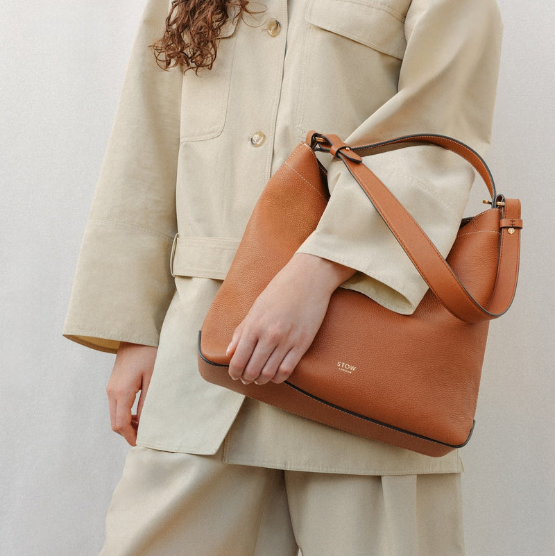 Model wearing STOW London's Curve in Earth Tan leather featuring the detachable shoulder strap with gold hardware and details 