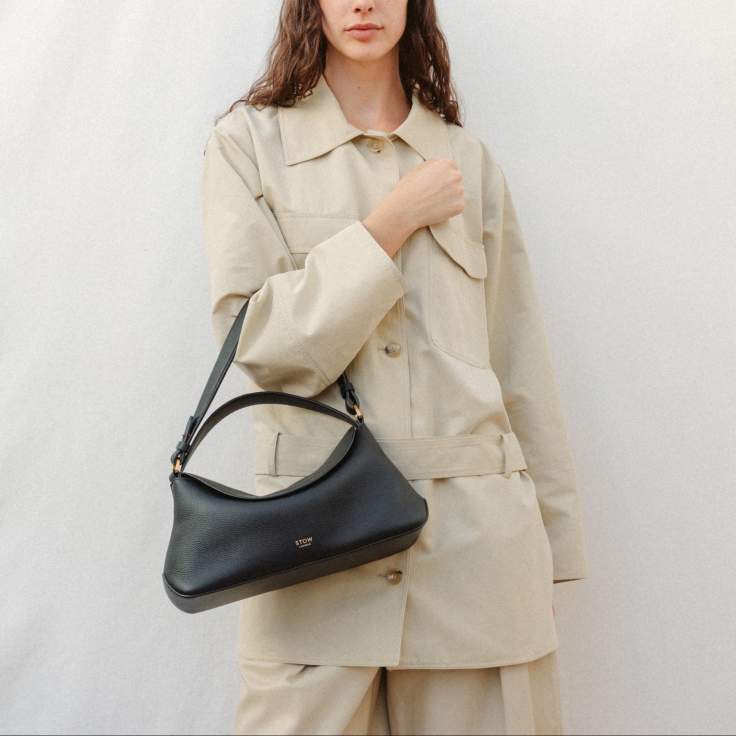 Model wearing STOW London's East West and detachable shoulder strap in Black leather featuring gold hardware and details 
