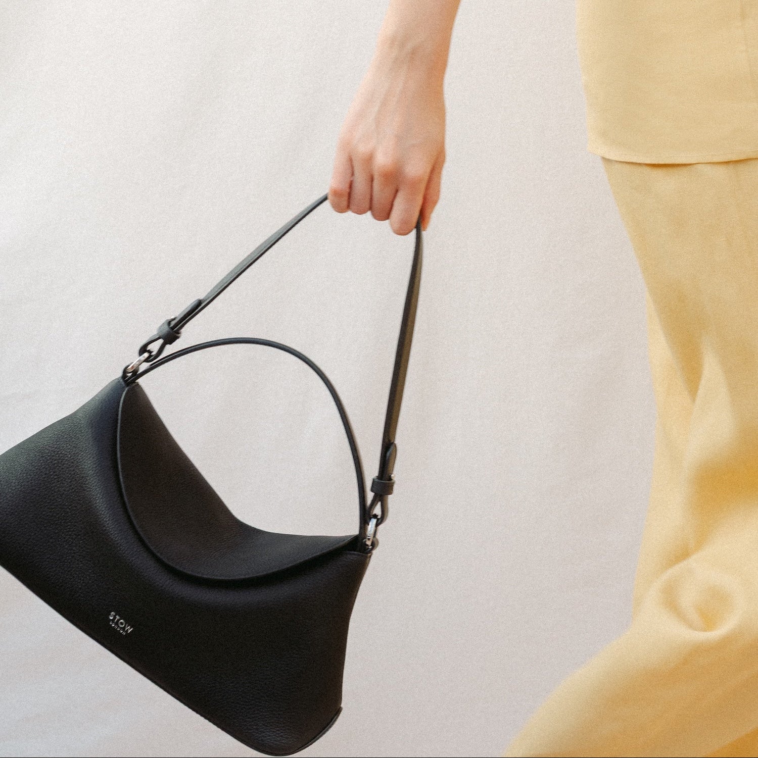 Model holding STOW London's East West and detachable shoulder strap in Black leather featuring silver hardware and details 