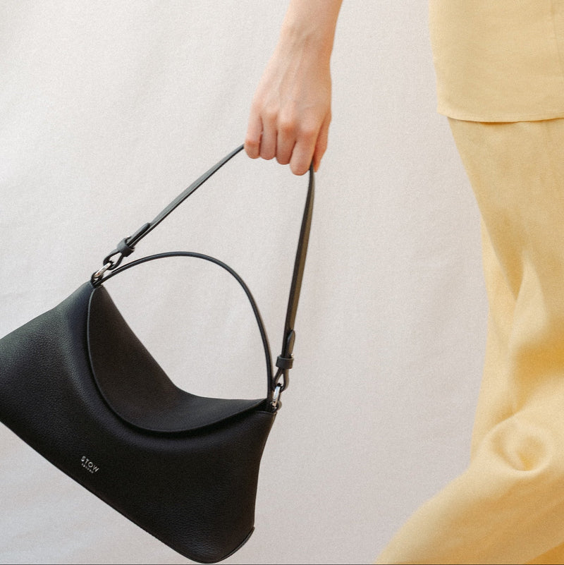 Model holding STOW London's East West and detachable shoulder strap in Black leather featuring silver hardware and details 