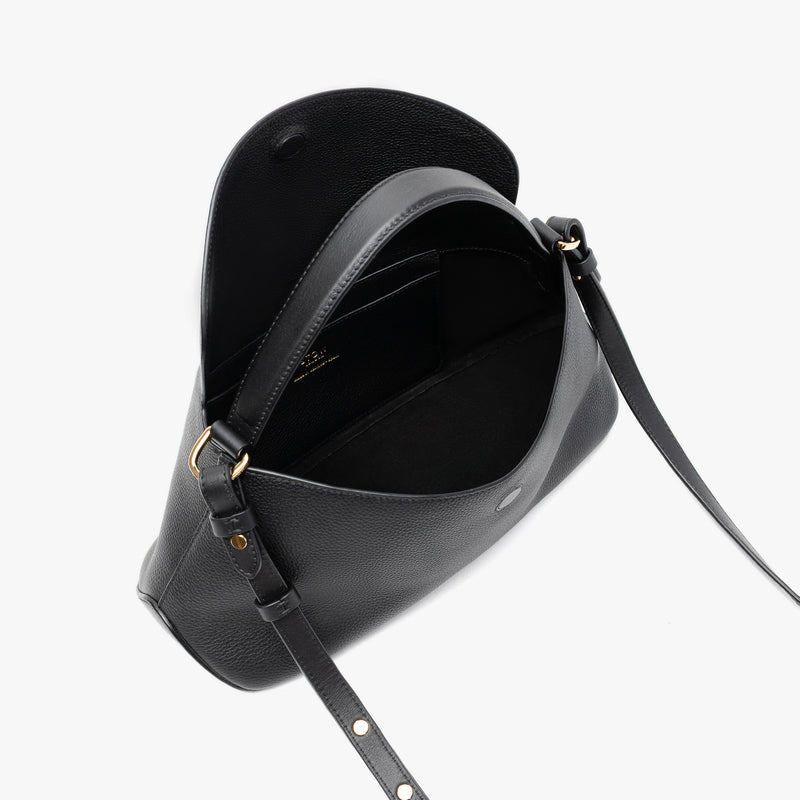STOW London's East West in Black pebbled leather with flap open showing black suede interior and slip pocket featuring gold-coated stainless steel hardware on a light grey background