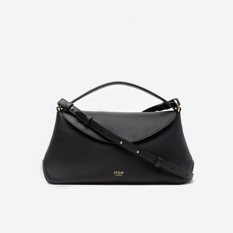 STOW London's East West in Black pebbled leather and detachable crossbody strap featuring gold-coated stainless steel hardware on a light grey background
