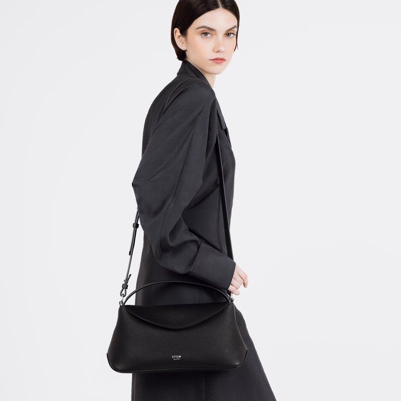 Model wearing STOW London's East West bag in Black pebbled and smooth leather on her shoulder featuring silver stainless steel hardware on a white background